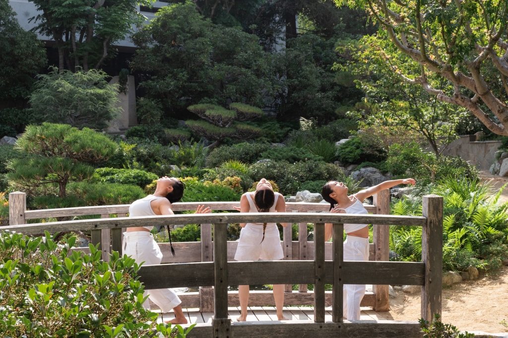 Three BIPOC dancers on a wooden bridge in Japanese Garden.