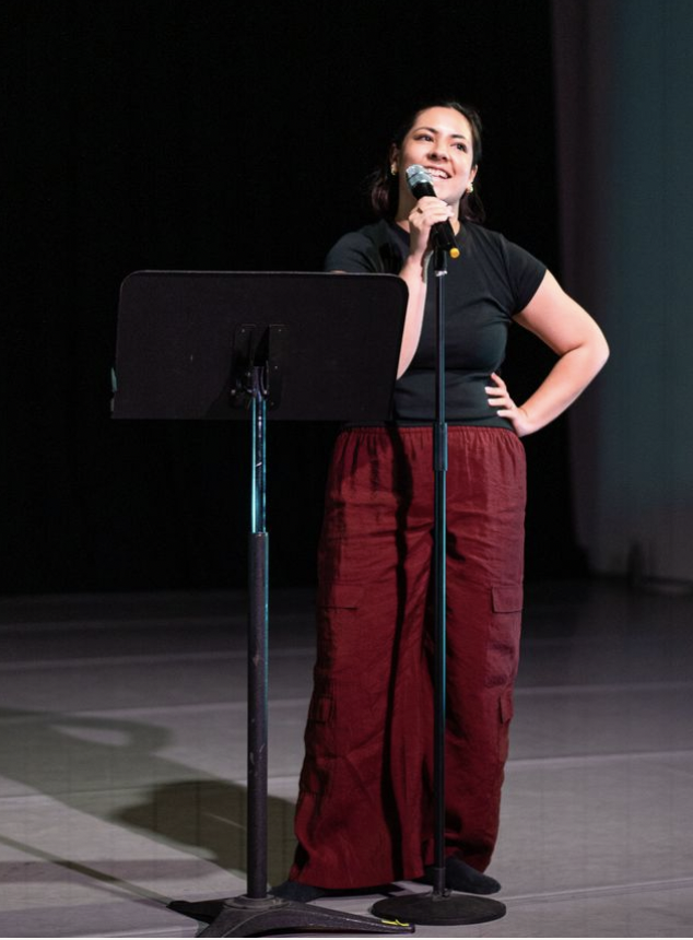 Female dancer standing behind a microphone and music stand smiling as she talks to the audience. 