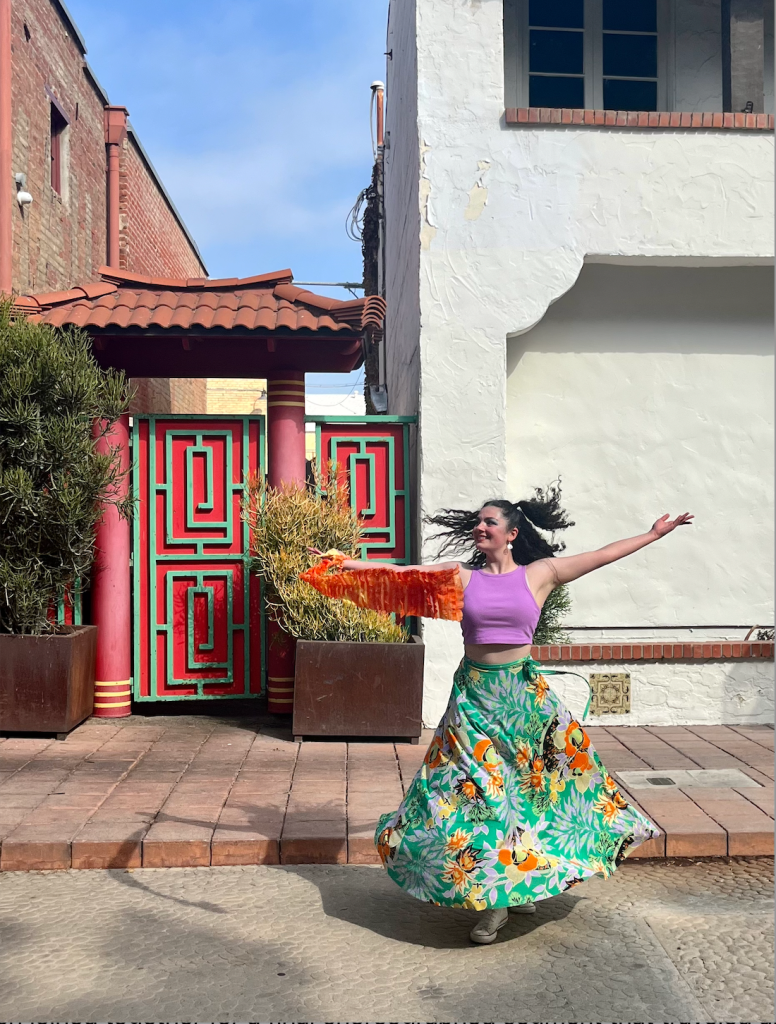Smiling dancer spinning in a long colorful dress with outstretched arms. 