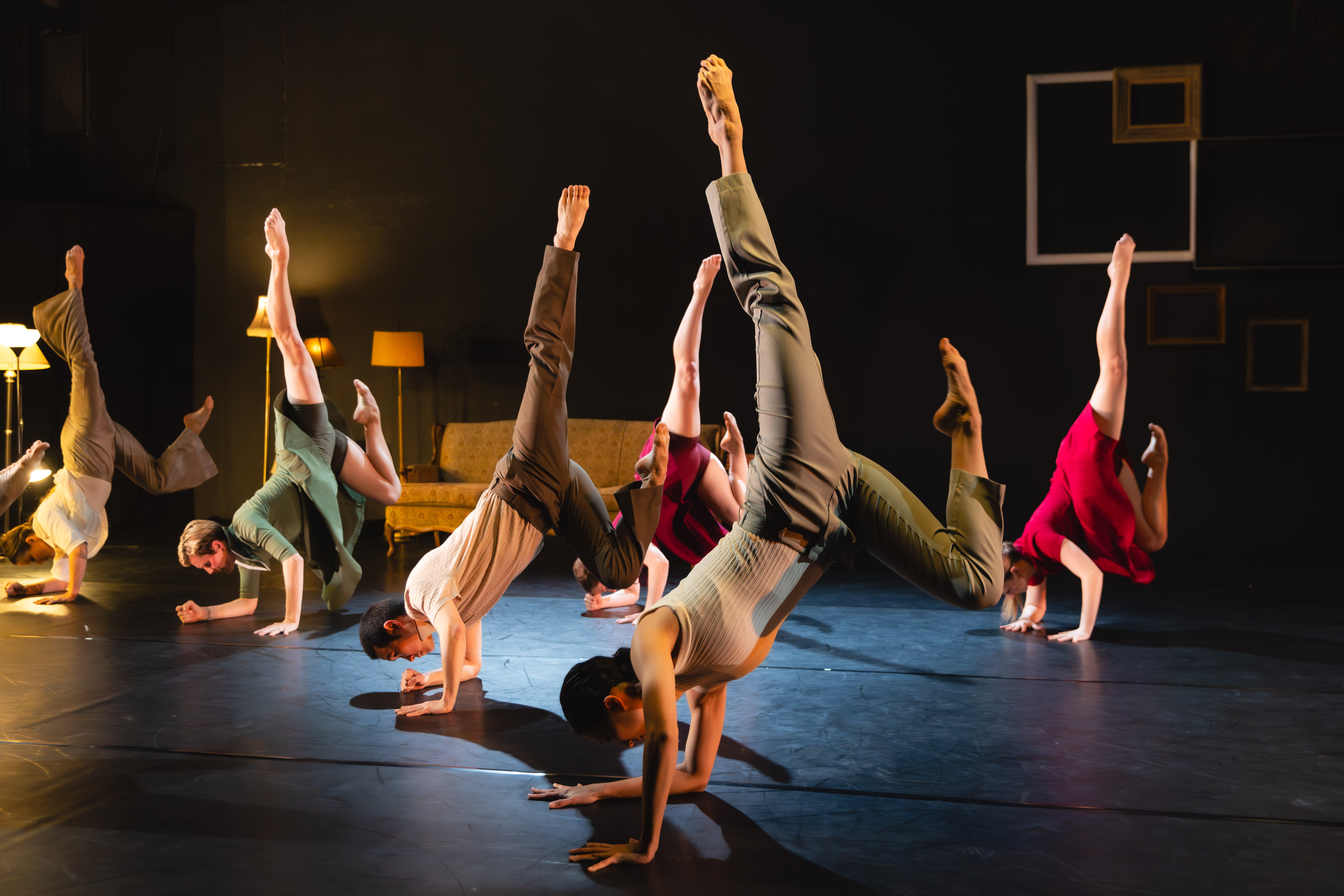Ensemble of dancers supporting on one hand and one elbow with both legs kicked vertically into the air.
