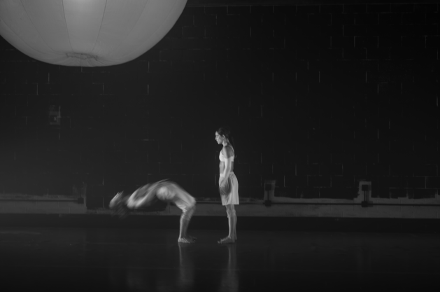 Two dancers. One arching back while the other stands watching.